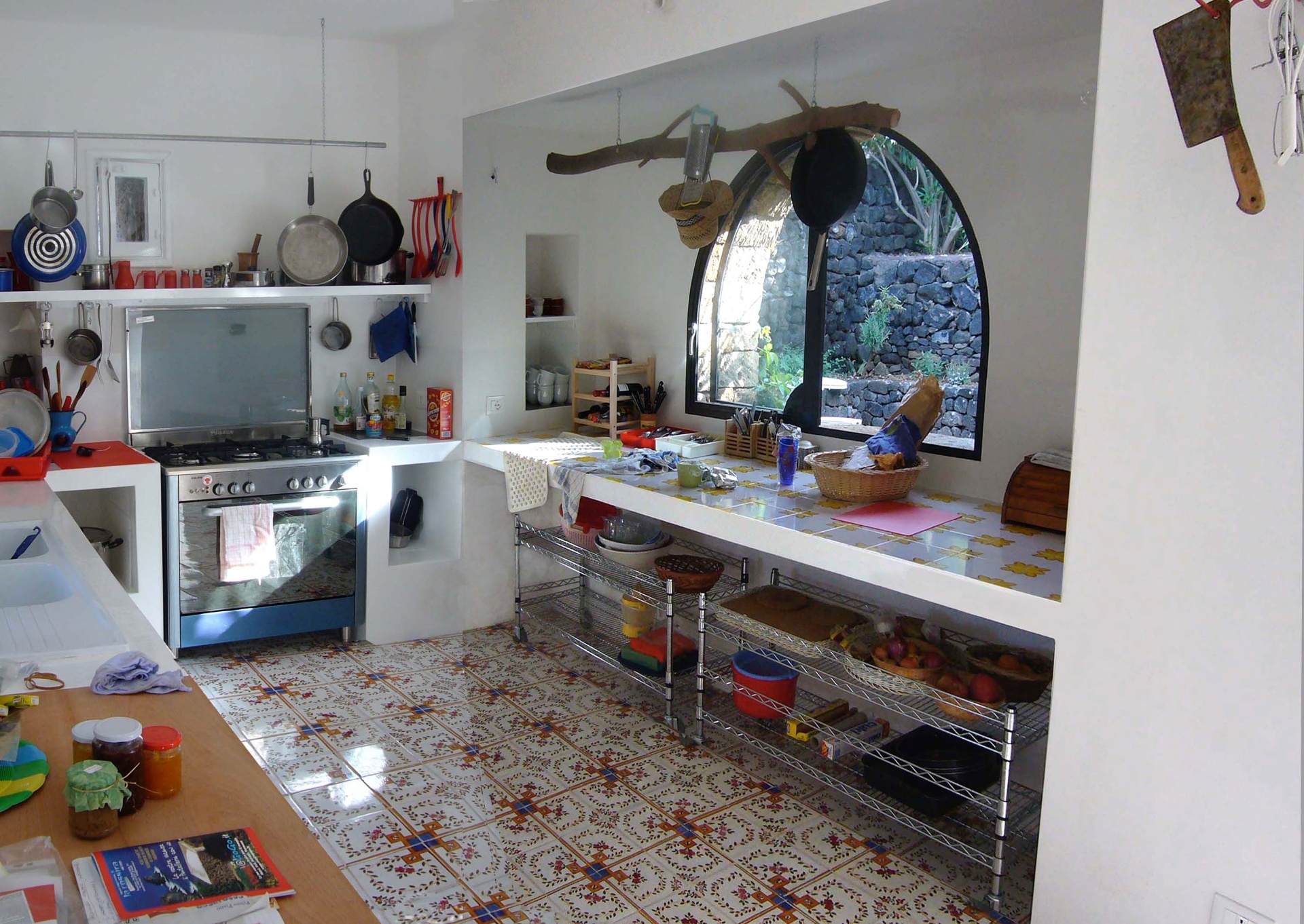 Stone dwelling kitchen with gas range, hanging cookware, arched window and patterned tile floor