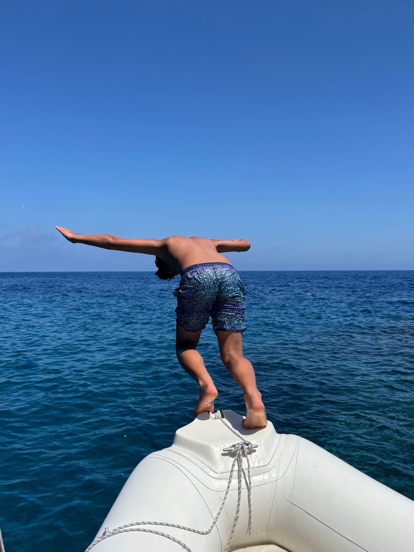 Young diver leaping from the bow of a dinghy into the deep blue sea