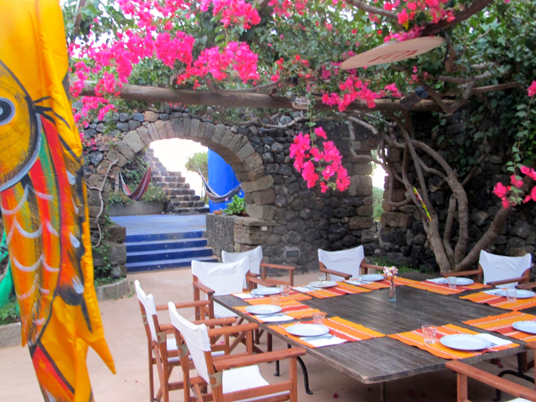 Outdoor dining table under bougainvillea pergola with blue patio archway in the background