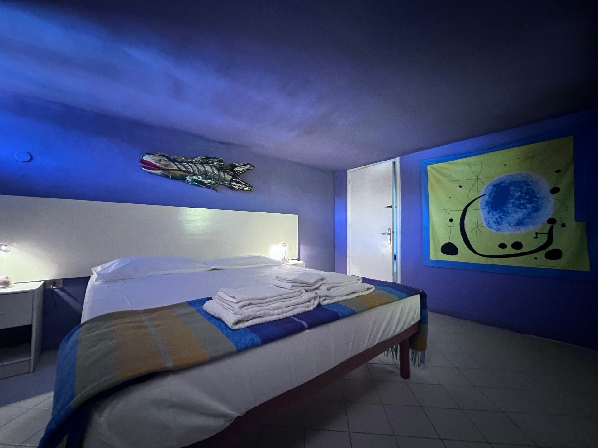 Mexican Suite with blue walls, double bed, striped blanket, and Miró-style tapestry