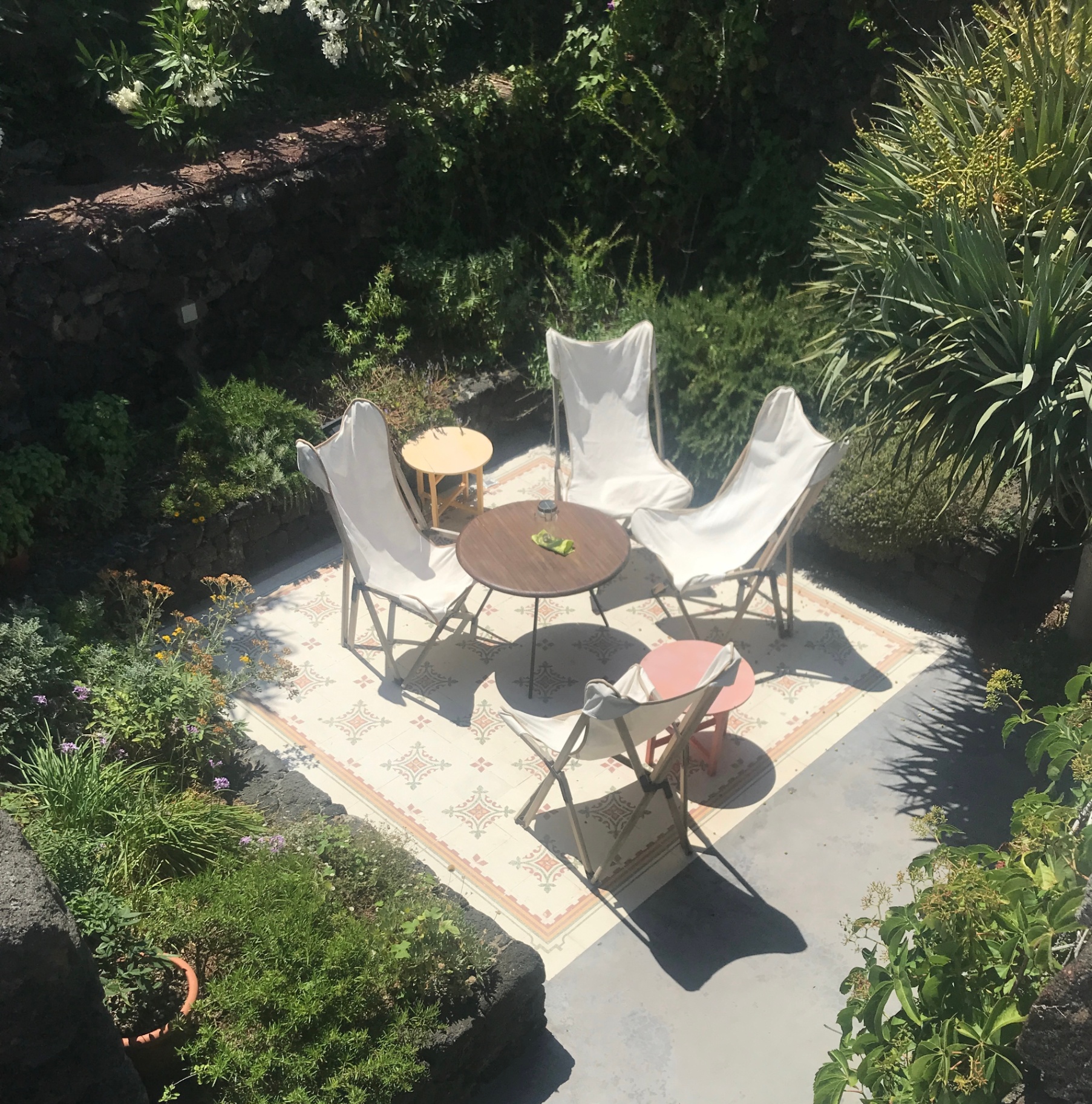 Patio delle Spezie with butterfly chairs on patterned tile rug surrounded by lush garden