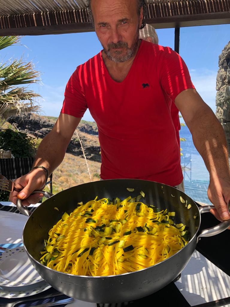 Local chef presenting a pan of yellow tagliolini with zucchini overlooking the sea