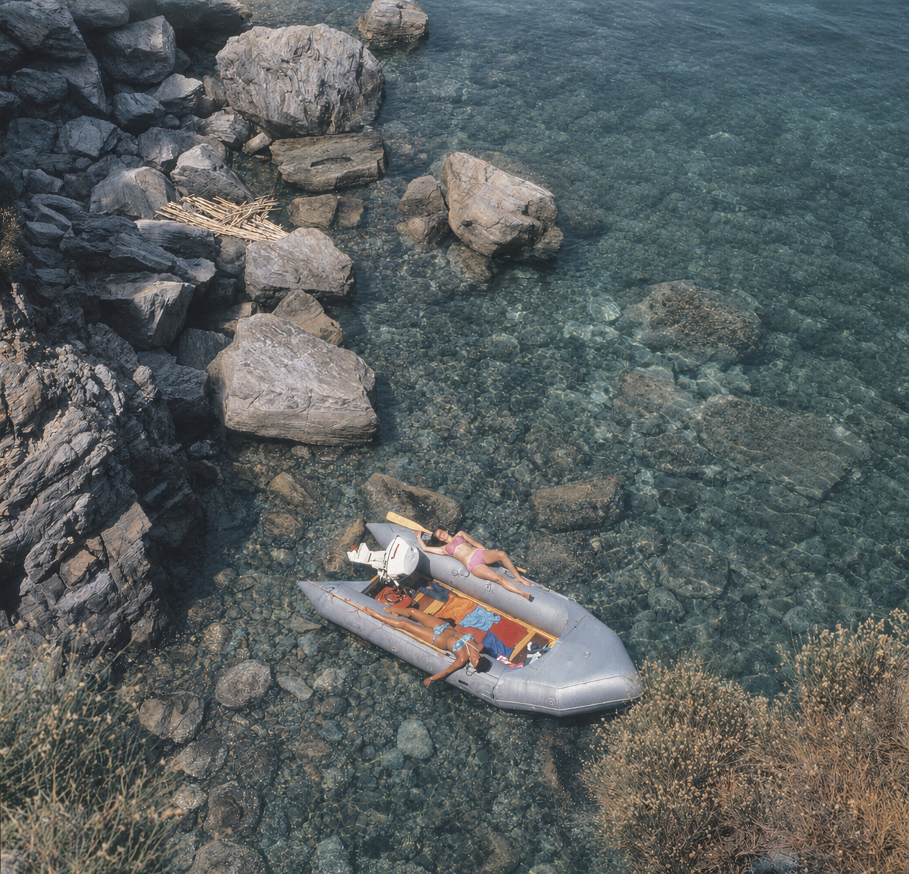 Aerial view of a dinghy in crystal-clear water along a rocky shore