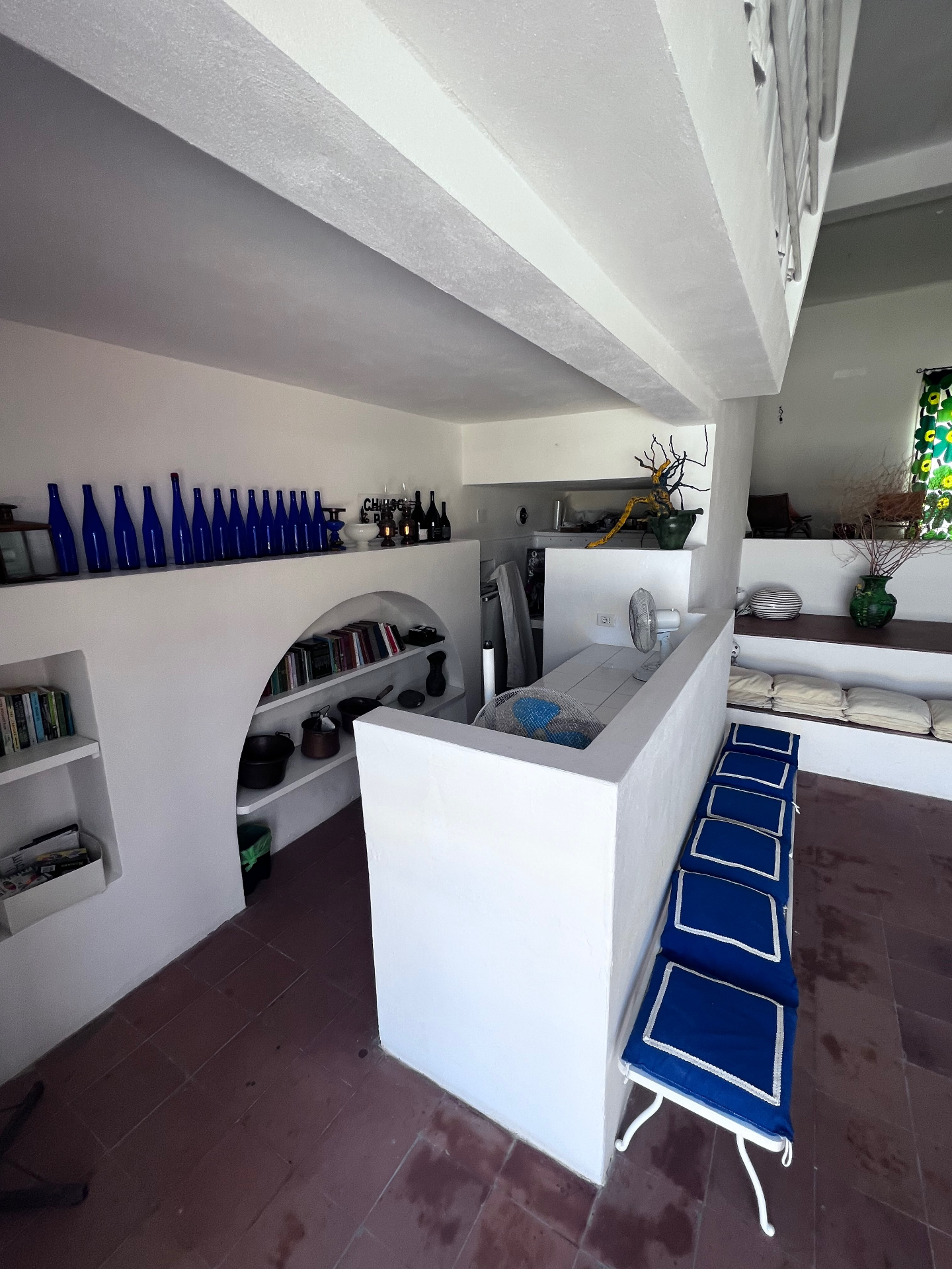Kitchenette with arched bookshelf niche, blue glass bottles, and blue cushioned bench