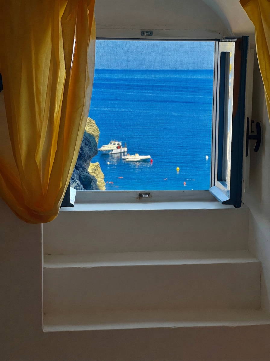 View of Cala Tramontana through a bedroom window with yellow curtains