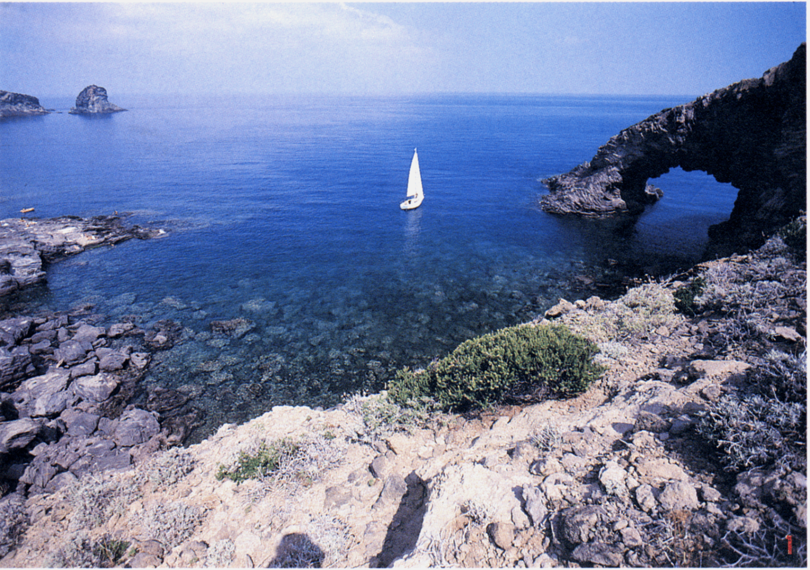 Sailboat passing a natural lava arch along Pantelleria's coastline