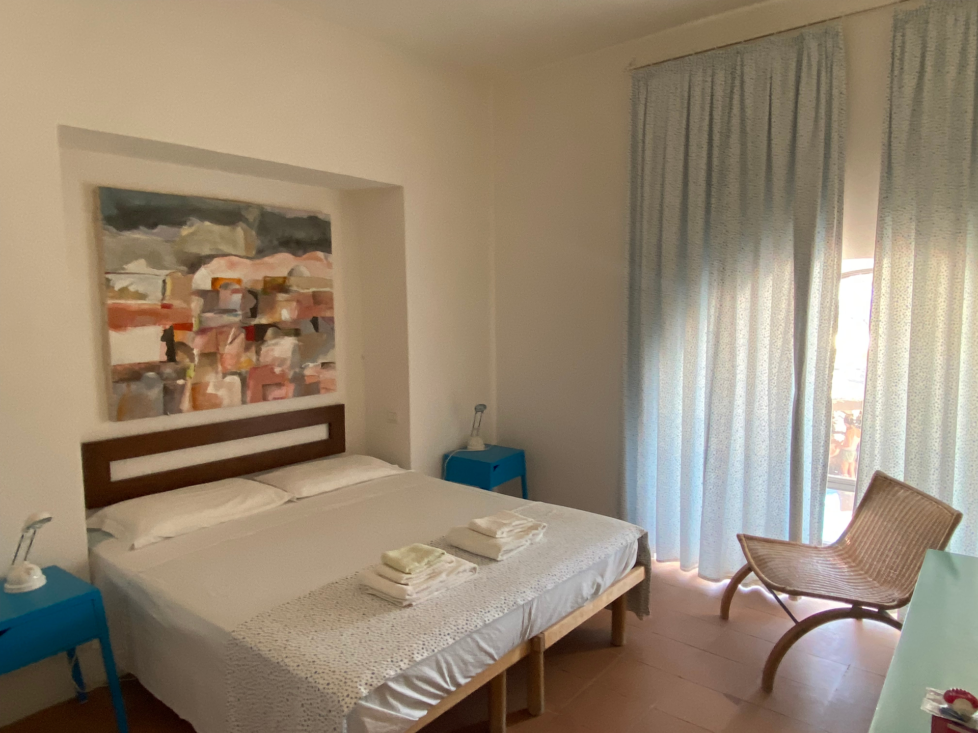 Royal Suite bedroom with double bed, abstract painting, blue nightstands, and rattan lounge chair
