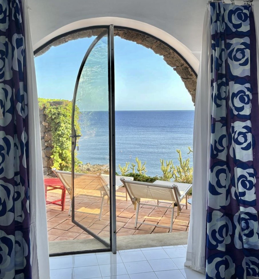 View through arched glass door onto terrace with loungers and sea beyond